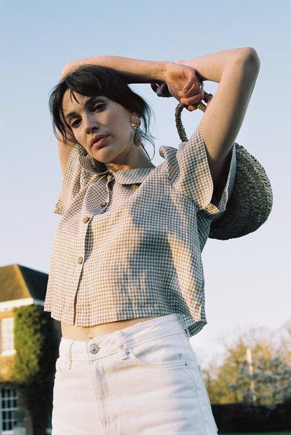 Woman wearing a checkered shirt and white pants with a straw hat, standing outdoors.