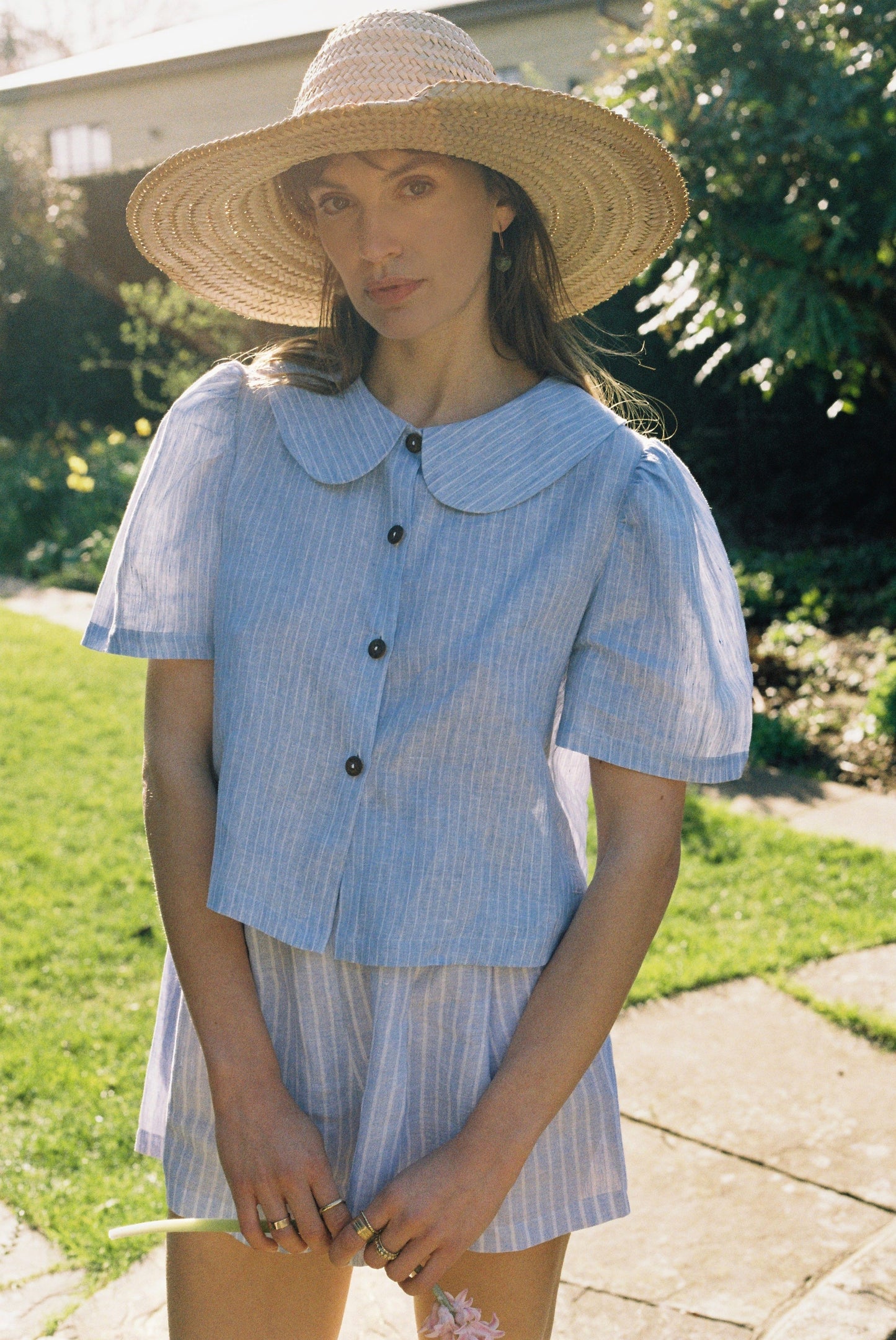 Woman wearing a blue checkered dress with a wide-brimmed hat outdoors.