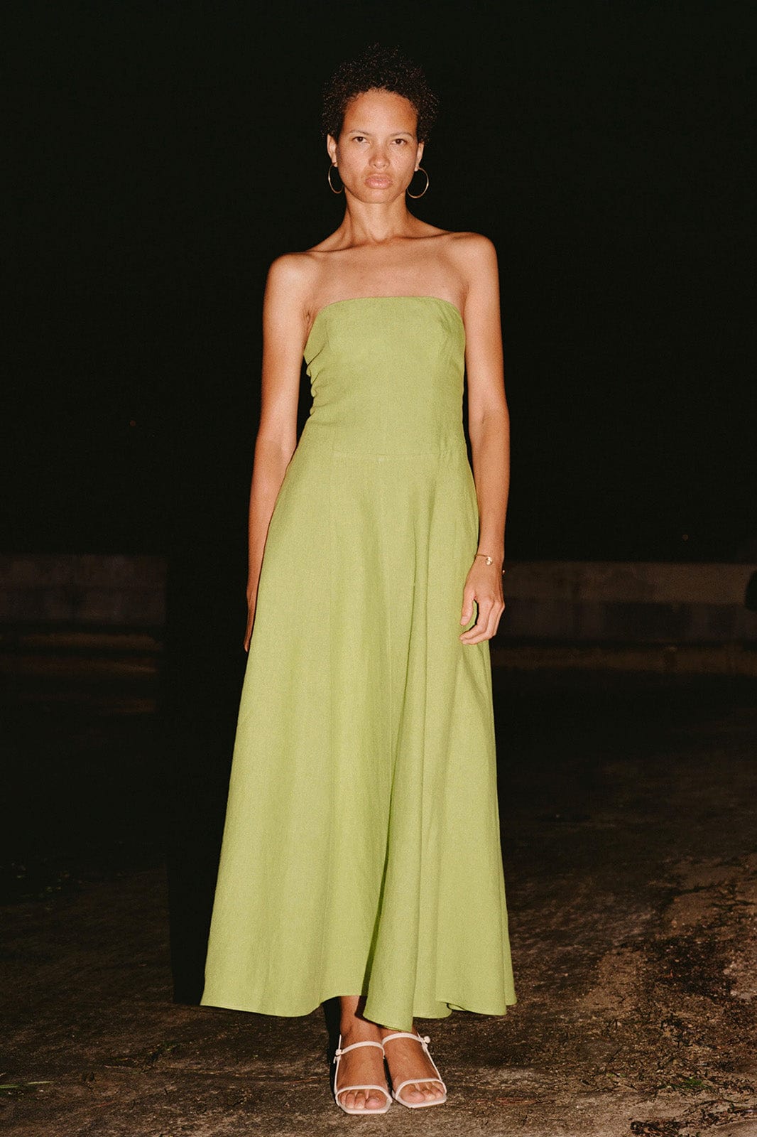 Woman wearing a strapless green dress standing against a dark background
