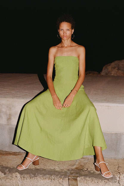 Woman in a green strapless dress sitting on a stone bench at night.