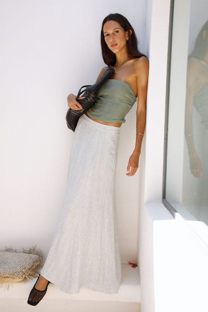 Woman wearing a green top and white skirt standing against a white wall.