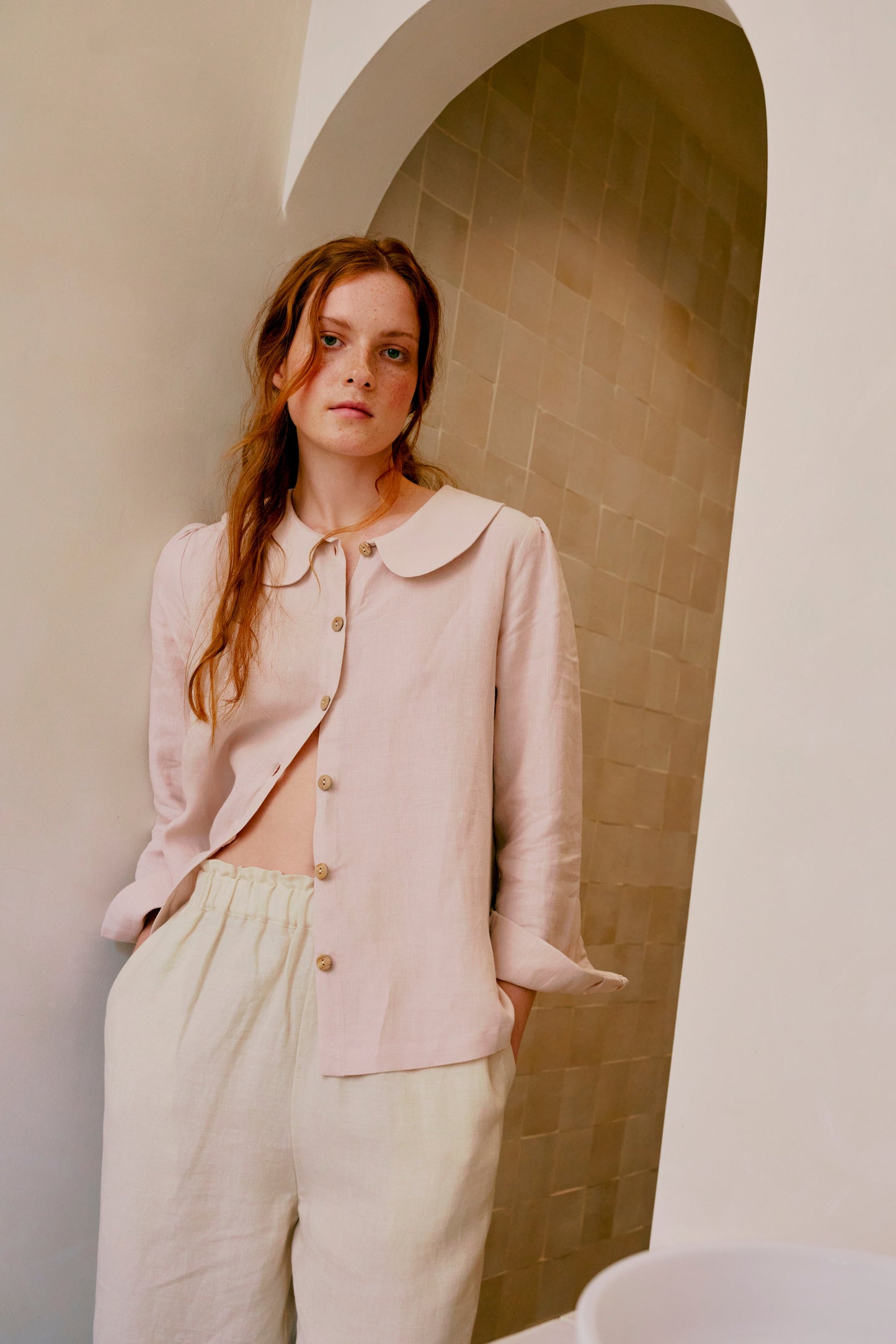 Woman wearing a light pink jacket and beige pants in a bathroom setting