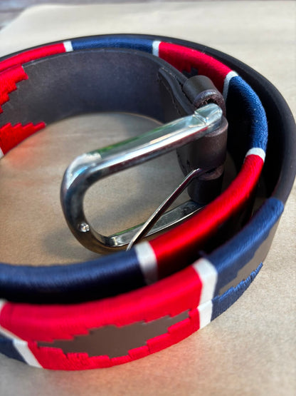 A close-up of a woven belt with a red, white, and blue pattern, a dark gray center, and a silver metal buckle, coiled on a neutral surface.