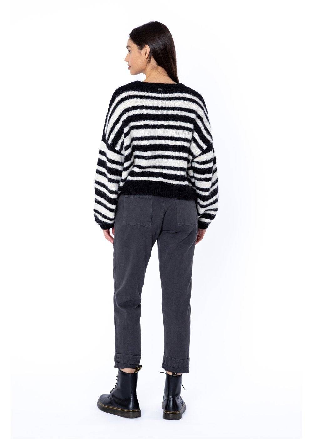 Woman wearing a striped sweater and dark trousers on a white background from the back