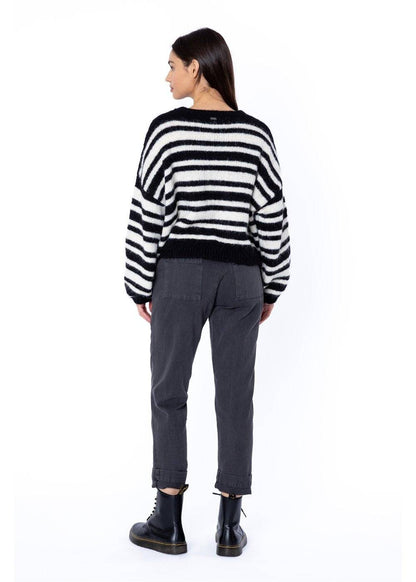 Woman wearing a striped sweater and dark trousers on a white background from the back