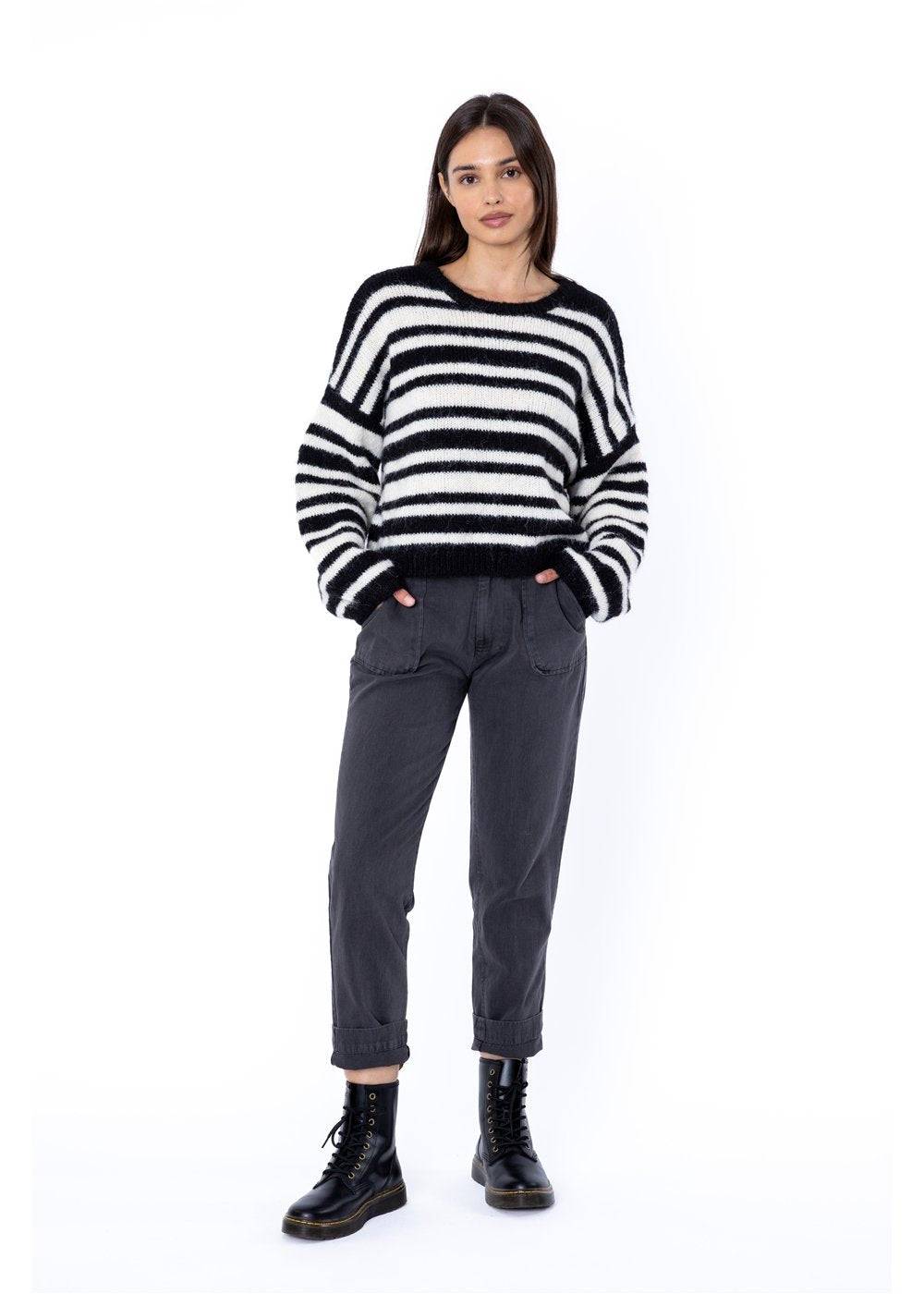 Woman wearing a striped sweater and dark trousers on a white background
