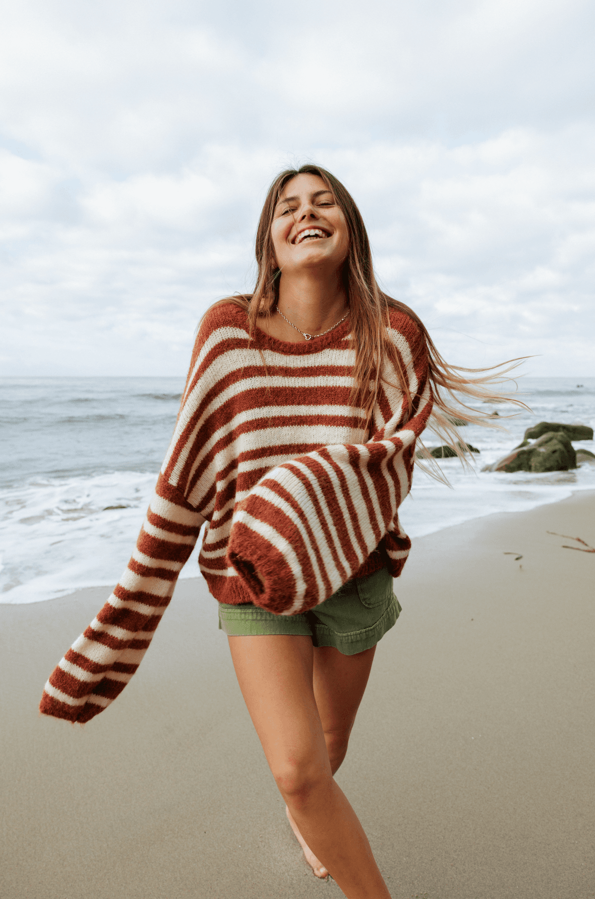 Woman wearing a striped sweater and green shorts on a white background on the beach